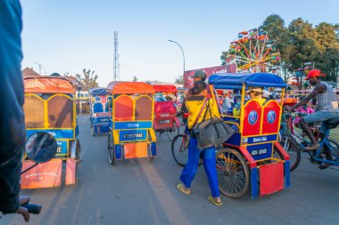 Antsirabe, Madagaskar - 30 Ağustos 2024: Bu dağlık şehirde dönme dolabın yanında renkli geleneksel rickshaws kuyruğu var. Bu triportörler Antsirabe 'de popüler bir turist taşımacılığıdır..