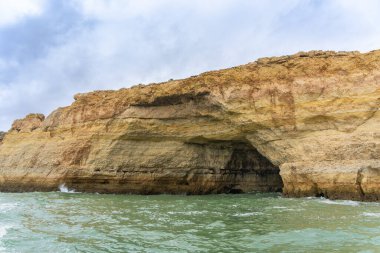 Alacakaranlıkta, zümrüt sularının üzerinde karmaşık deniz mağaralarıyla birlikte Altın Kıyı uçurumları yükseliyor. Dalgalar, Algarve ve Portekiz tarafından şekillendirilen şaşırtıcı kaya oluşumları.