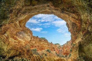 Benagil Mağarası 'ndaki tavan penceresinin nefes kesen manzarası doğal kaya oluşumlarını ve yukarıdaki mavi gökyüzünü gözler önüne seriyor. Bu ünlü deniz mağarası eşsiz güzelliğiyle bilinir. Algarve, Portekiz.