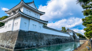 Nijo Kalesi 'nin taştan duvarlarını nazikçe geçen sakin bir su yolu, kalenin zarif beyaz cephesini ve karmaşık mimarisini yansıtıyor. Kyoto, Japonya.