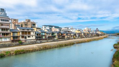 Geleneksel Japon evleri Kyoto 'daki Kamo Nehri kıyısında yer alır. Huzurlu sahne, arka planında modern binalar bulunan eski ve yeni arasında güzel bir kontrastlık sunuyor. Kyoto, Japonya.