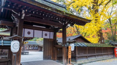 Kyoto, Japonya - 9 Aralık 2024 Kawai Tapınağı 'nın beyaz fenerler ve sancaklarla süslenmiş ana kapısı renkli bir sonbahar yeşilliğine karşı duruyor..