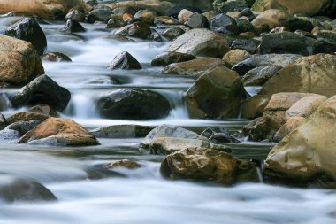 Düz kayaların üzerinden akan sakin bir nehir. Su uzun süre maruz kaldığı için ipeksi görünüyor, sakin bir manzara yaratıyor. Wulai Bölgesi, New Taipei Şehri, Tayvan.
