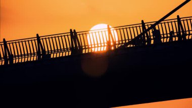 Canlı turist günbatımında Aşıklar Köprüsü 'nde siluetli turistler. Güneş köprünün arkasında batıyor, dramatik gölgeler bırakıyor. Tamsui Balıkçı Rıhtımı, New Taipei Şehri, Tayvan.