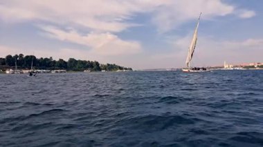 Nil Nehri kıyısı boyunca filikalar ve motorlu tekneler de dahil olmak üzere çeşitli tekneler demirlemiştir. Yeşil ağaçlar ve binalar kıyı boyunca uzanır, Aswan, Mısır 'da sakin bir manzara yaratır..