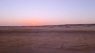Basit çizgiler, otobüs penceresinden çölün doğuşunu yakalıyor. Şafak ışığı, sabah otobüsü yolculuğu sırasında Mısır 'ın Aswan kentindeki kumlu araziyi aydınlatır..