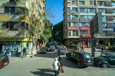 Kahire, Mısır - 13 Ocak 2025: Kahire 'de bir tur otobüsünden yayalar, park edilmiş arabalar ve çeşitli dükkanları ve tabelaları olan binalar görüntülenmiş hareketli bir sokak görüntüsü.