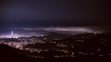 Tayvan 'daki Lion Head Dağı' ndan Taipei 'nin bahar gecesi manzarası. Alçak bulutlar sola hareket eder, yüksek bulutlar aydınlık şehrin üzerinde hareket eder..