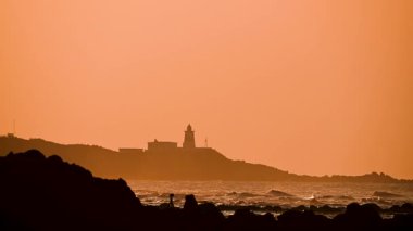 Shimen, New Taipei City, Tayvan 'da bir bahar akşamı sahnesi. Gün batımı, dalgalar ve deniz feneri manzarası. Ayrıntılı manzara görüntüsü.