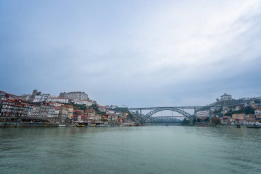 Porto 'nun renkli nehir kenarı binaları ve Douro Nehri' ni kaplayan ikonik Dom Luis Köprüsü 'nün bulutlu bir öğleden sonra manzarası..