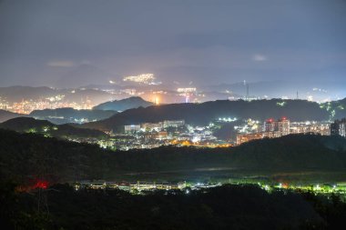 Ruifang, New Taipei City, Tayvan 'ın göz kamaştırıcı gece manzarası. Görüntü, kentin aydınlık binalarını ve altyapısını kayan tepeler ve uzak ışıklara karşı sergiliyor.