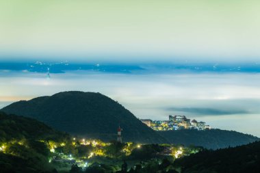 Tayvan 'ın Taipei şehrinde Datun Dağı' nda, yoğun sis ile kısmen gizlenmiş bir dağın tepesindeki üniversite binalarının gece görüşü. Binaların ışıkları sisin içinde parlıyor..