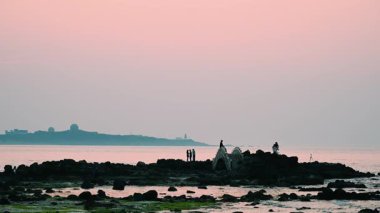 Gün batımında, Shimen, New Taipei, Tayvan 'ın sakin güzelliğini kayalık sahillerin tadını çıkaran turistlerle yakalayın. Seyahat ve doğa temaları için mükemmel..