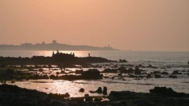 Shimen, New Taipei City, Tayvan 'ın kayalık sahillerinde toplanan turistler, güzel günbatımını okyanus üzerinde yakalıyorlar..