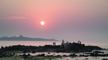 Gün batımında, Shimen, New Taipei, Tayvan 'ın sakin güzelliğini kayalık sahillerin tadını çıkaran turistlerle yakalayın. Seyahat ve doğa temaları için mükemmel..