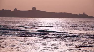 Yavaş çekim, Shimen, New Taipei City, Tayvan 'da gün batımında sakin ve pırıl pırıl bir sahne yaratan altın dalgaları yakalar..