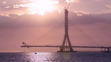 Tamsui, New Taipei City, Tayvan 'da su üzerinde kablo destekli köprü inşaatının dramatik günbatımı manzarası. Altın saat aydınlatma çarpıcı bir siluet yaratır.