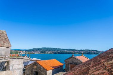 Bu görüntü İspanya 'nın Combarro kentindeki güzel kıyı kasabasını, kırmızı kiremitli çatıları ve deniz manzarası ve çevresindeki tepelerle geleneksel Galiçya mimarisini yansıtıyor..