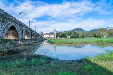 Ponte de Lima köprüsü Portekiz 'in sakin sularında, mavi gökyüzünün altında mükemmel bir yansıması var. San Antonio Kilisesi karşı kıyıdan görülebilir..