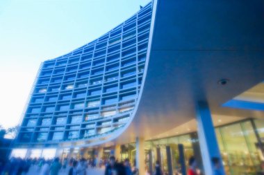 Taipei, Tayvan - 13 Ekim 2013: Songshan Kültür ve Yaratıcı Park 'ta günbatımına karşı görülen modern eğimli bir bina. İnsanlar aydınlanmış yapının önünde toplanıyor..