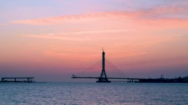 Tamsui Nehri Köprüsü 'nün silueti New Taipei City, Tayvan' da gün batımında yapım aşamasında. Pembe ve turuncu gün batımı gökyüzü ve yumuşak deniz dalgaları.