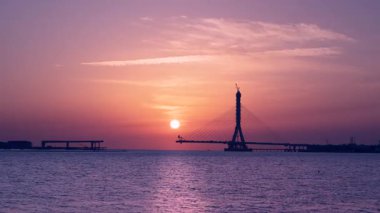 Günbatımı, New Taipei City, Tayvan 'da inşa halindeki Tamsui Nehri Köprüsü üzerinde pembe ve turuncu tonlarda gökyüzünü boyar. Sakin sular renkli gökyüzünü yansıtır..
