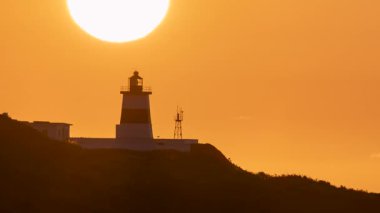 New Taipei City, Tayvan 'daki Shimen Deniz Feneri' nde büyüleyici bir gün batımı. Güneş fenerin arkasında batıyor ve turuncu gökyüzü parlıyor..