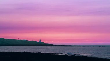 Shimen, New Taipei City, Tayvan 'daki Fuguei Burnu' nun üzerinde canlı pembe ve turuncu renkleri olan büyüleyici bir romantik gökyüzü. Uzak deniz feneri aralıklı kirişini atar.