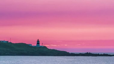 Tayvan 'ın New Taipei şehrinde Shimen Deniz Feneri' nin üzerinde parlayan pembe-turuncu bir günbatımı gökyüzü alacakaranlıkta hafifçe yanıp sönüyor..