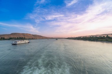 Mısır 'ın Aswan kentindeki Esna Kilidi yakınlarındaki Nil Nehri' nde sakin bir manzara. Yumuşak, renkli gökyüzü ve uzak çöl kıyılarıyla dolu güzel bir alacakaranlıkta iki yolcu gemisi sularda yüzüyor..
