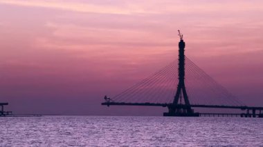 Danjiang Köprüsü 'nün yeni Taipei şehrindeki pembe-turuncu gökyüzü ve yumuşak deniz dalgalarıyla inşa edildiği huzurlu günbatımı manzarası..