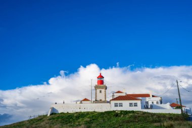 Portekiz 'in Avrupa anakarasının en batı noktasında bulunan İkonik Cabo da Roca deniz feneri, beyaz bulutlu dramatik mavi gökyüzüne karşı kurulmuştur..