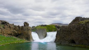 İzlanda 'daki kendine özgü Hjalparfoss şelalesi, sert bazalt sütunlarıyla çerçevelenmiş, güçlü ikiz şelaleleri temiz bir havuza düşüyor..
