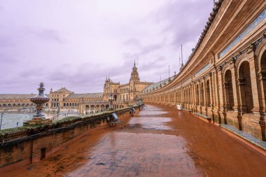 İspanya 'daki Sevilla Plaza de Espana, yağmurlu bir bahar alacakaranlık gökyüzünün altında süslemeli mimari ve renkli fayanslarla serinleten bir çeşme gösteriyor..