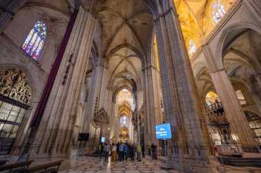 Sevilla, İspanya - 10 Mart 2025: Geniş iç kısımda uzun kemerler ve boyalı camlar. Ziyaretçiler, uzayı rehberli tur işaretleriyle keşfediyorlar. En büyük Gotik katedral ve UNESCO sitesi.