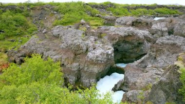 Yaz boyunca İzlanda 'daki Barnafoss şelalelerinin hava manzarası. Beyaz akıntılar, engebeli volkanik kaya oluşumlarının içinden akan turkuaz buzul suyuyla karşılaşıyor..