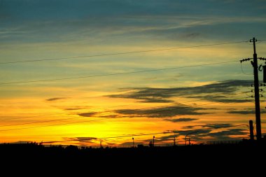 Canlı bir günbatımı, Tayvan 'ın Miaoli kentindeki Longgang Limanı yakınlarındaki kırsal arazinin üzerinde siluetli elektrik direkleriyle ve sokak lambalarıyla gökyüzünü sıcacık renklerle boyuyor..