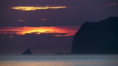 Waimushan Keelung Tayvan 'da güneşin Keelung Adası üzerindeki dramatik bulutların arasından doğuşu sakin okyanusta altın turuncu yansımalar yaratıyor..