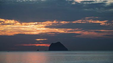 Güneş, Keelung Adası 'nın arkasındaki dramatik bulutların arasından yükseliyor. Tayvan Waimushan sahilinden sakin okyanusun üzerine altın ve turuncu ışık saçıyor..