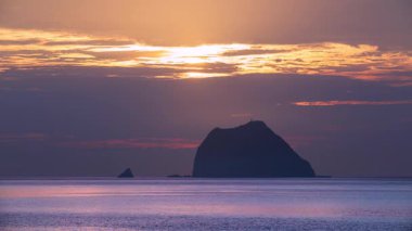 Waimushan Keelung Tayvan 'da güneşin Keelung Adası üzerindeki dramatik bulutların arasından doğuşu sakin okyanusta altın turuncu yansımalar yaratıyor..