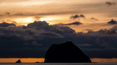 Tayvan, Keelung Waimushan 'da çarpıcı bir yaz gündoğumu. Güneş, hızlı hareket eden kara bulutlar tarafından gizlenir ve sakin denizin üzerinde dramatik bir sahne yaratır..