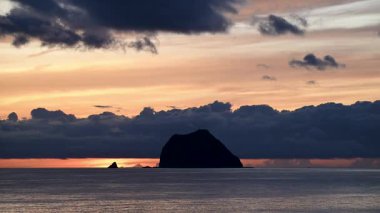 Tayvan, Keelung Waimushan 'da çarpıcı bir yaz gündoğumu. Güneş, hızlı hareket eden kara bulutlar tarafından gizlenir ve sakin denizin üzerinde dramatik bir sahne yaratır..