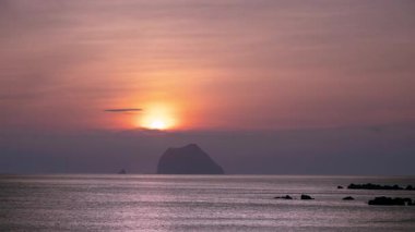 Keelung Waimushan, Tayvan 'da nefes kesici bir yaz gündoğumu. Güneş yavaşça kara bulutların arkasından çıkar, durgun bir denizin üzerinde güzel bir turuncu ışıltıyla gökyüzünü aydınlatır..