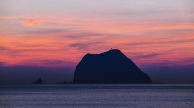 Waimushan Keelung Tayvan 'da şafaktan önceki büyülü sahne. Keelung Adası silueti çarpıcı pembe turuncu gökyüzüne karşı durgun okyanusta deniz feneri görünür..