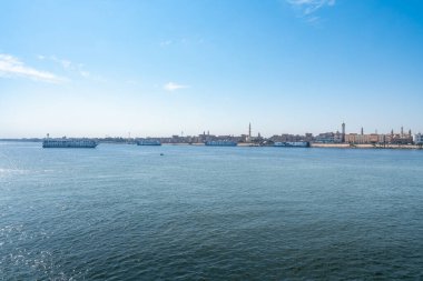 Esna 'ya giren yolcu gemilerinin huzurlu görüntüsü Mısır' daki Nil Nehri boyunca uzak şehir silueti ve minareleri ile açık mavi gökyüzünün altında kilitli..