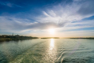 Alacakaranlıkta Esna Lock 'tan geçen bir Nil Nehri gezisi, sakin sulara ve nehir kenarındaki siluetlere yansıyan altın ışıkla birlikte. Mısır, 2025.