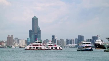 Kaohsiung Harbor, Taiwan - August 16, 2025: Passenger ferries and boats move across the water in a busy port city. The skyline features modern high-rise buildings.