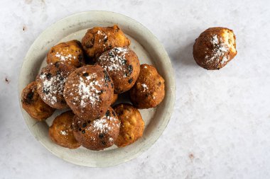 Beyaz arka planda bir bardak şampanyayla birlikte bir yığın oliebollen (tercüme: Hollanda hamur böreği) üst aşağı görünümü, bir oliebol ayrık, yatay