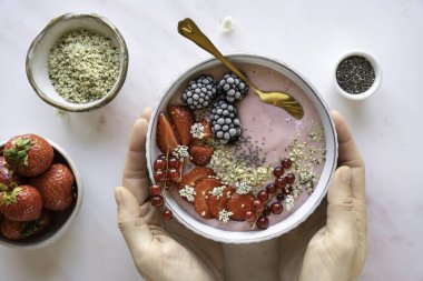 Meyveli, çilekli, böğürtlenli, elleri yatay tohumlu sağlıklı bir içecek kasesi.