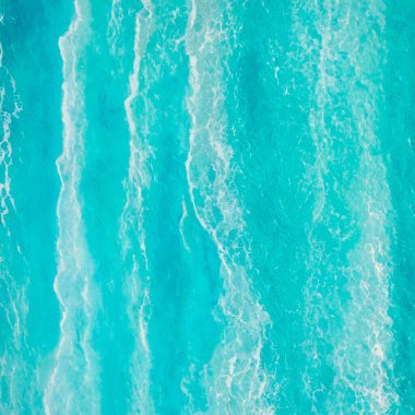 Mavi su, beyaz kum, dalgalar ve mavi su yüzeyiyle deniz kıyısının havadan görüntüsü..